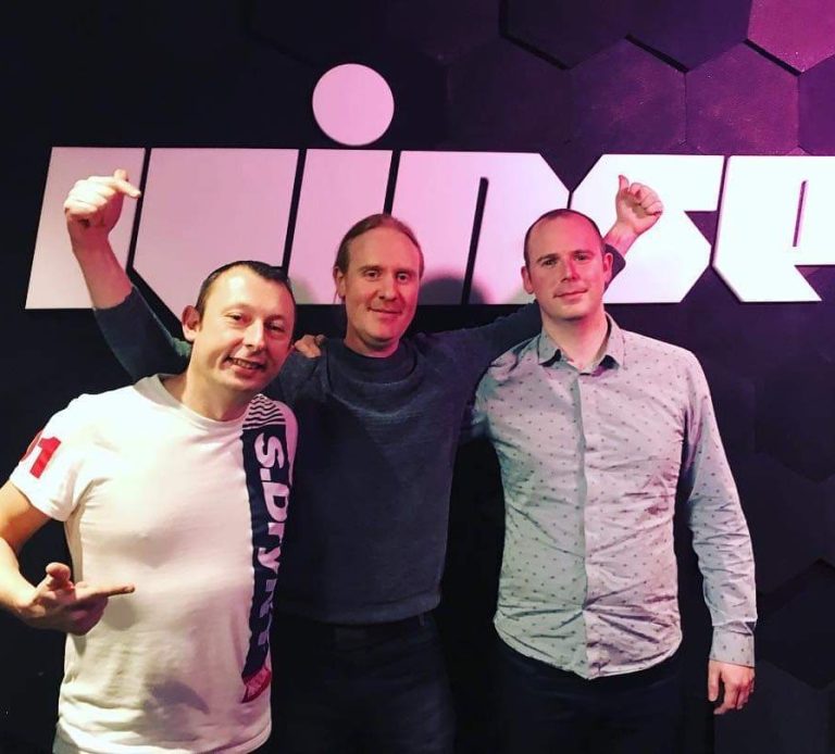Three men stand together, smiling, against a backdrop with the word "Rinse."